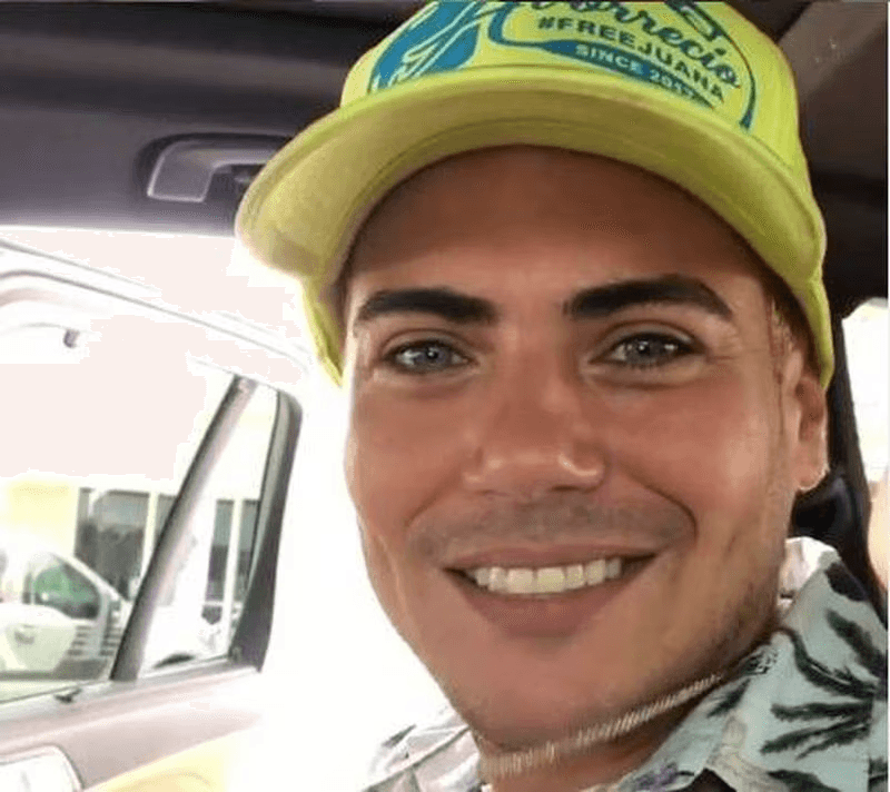 A smiling man wearing a yellow cap inside a car